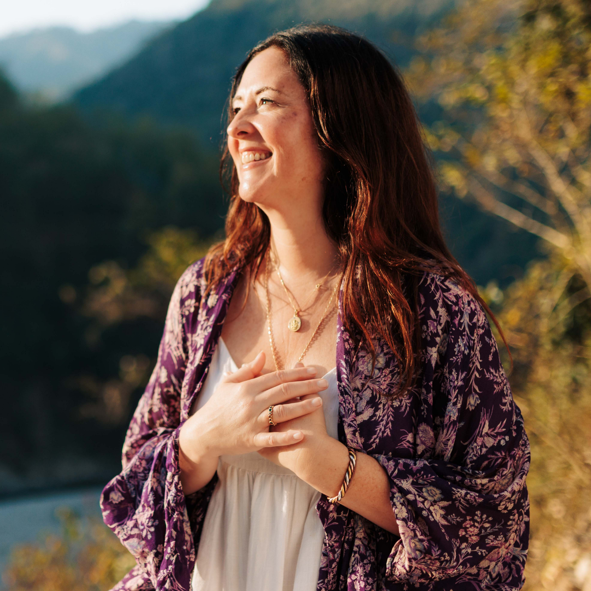 Woman standing outdoors with a scenic background of mountains and trees.